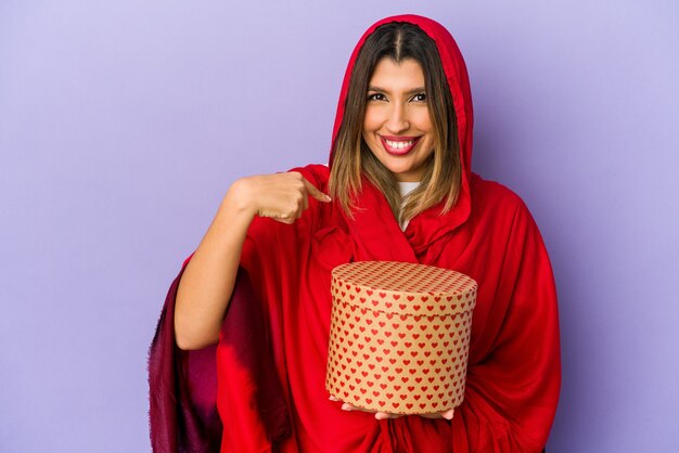 Jonge indische vrouw die een hijab draagt die een geïsoleerde valentijnskaartendaggift houdt die met de hand naar de ruimte van een overhemdskopie wijst, trots en zelfverzekerd