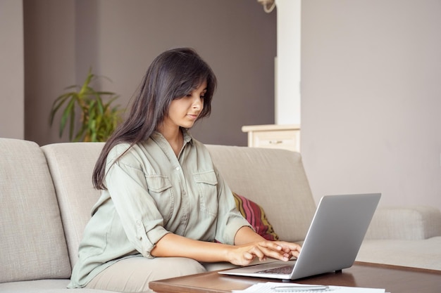 Jonge indische vrouw die laptopcomputer gebruikt die op kantoor aan huis werkt