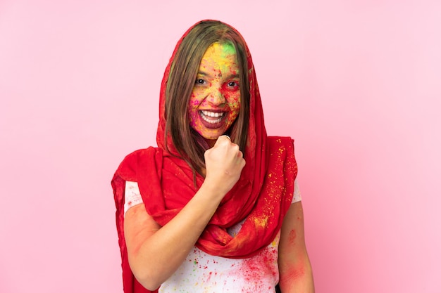 Jonge Indische vrouw die met kleurrijk holipoeder op haar gezicht op roze muur een overwinning viert