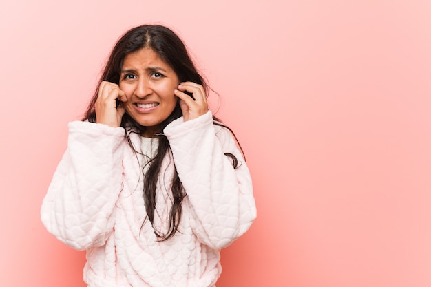 Jonge Indische vrouw die pyjama draagt die oren behandelt met zijn handen.