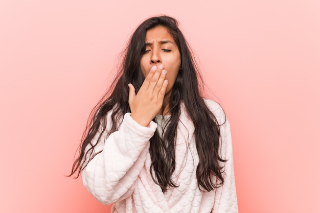 Jonge Indische vrouw die pyjama dragen die tonend een vermoeid gebaar tonen die mond behandelen met hem hand.