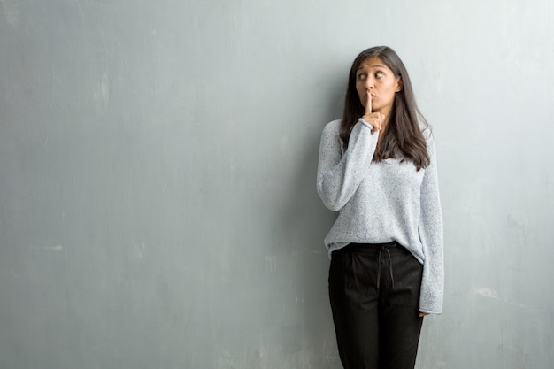 Jonge Indische vrouw tegen een grungemuur die een geheim houdt of om stilte vraagt