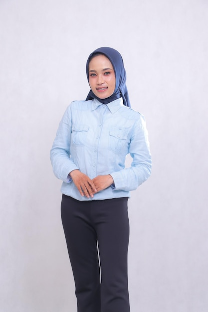 jonge indonesische kantoor meisje met blauw shirt hijab staande glimlachend vrolijk handen voor n