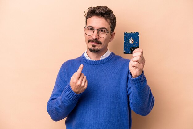 Jonge informaticaman geïsoleerd op beige achtergrond wijzend met de vinger naar je alsof uitnodigend dichterbij komt.