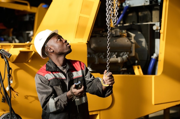 Foto jonge ingenieur die aan de ketting trekt terwijl hij een industriële machine bedient