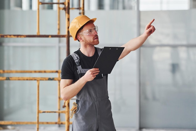 Jonge ingenieur in grijs uniform met notitieblok werkt overdag binnenshuis in een modern groot kantoor