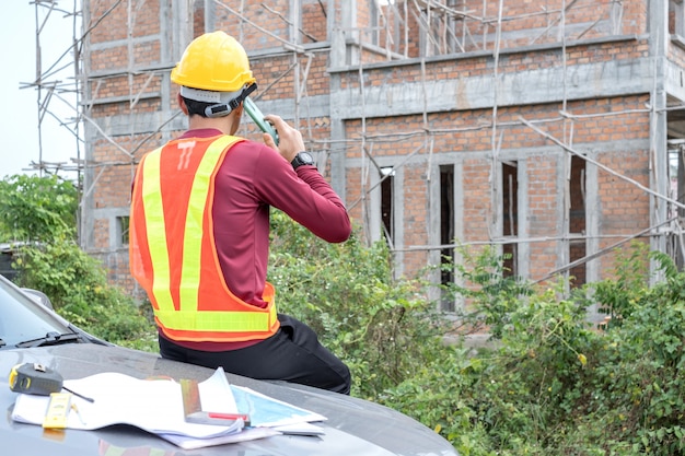 Jonge ingenieur praat met een telefoon voor een onvoltooid huis.