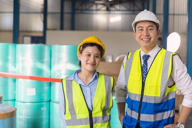 Jonge ingenieur werkende vrouw met volwassen man werknemer met veiligheidspak veiligheidshelm op fabrieksachtergrond