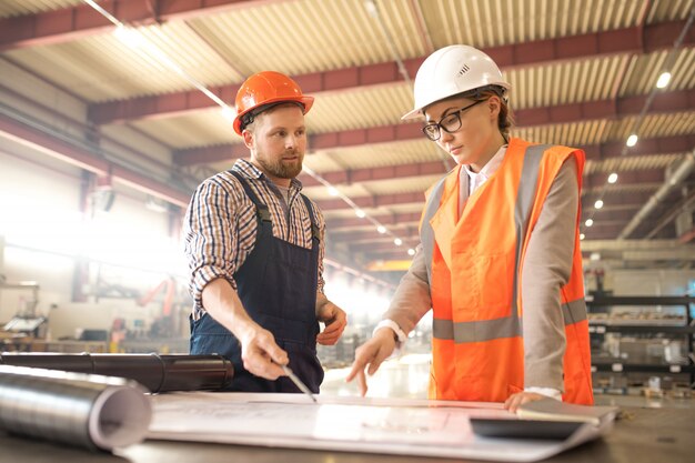 Jonge ingenieurs in werkkleding overleg over details van schets op blauwdruk tijdens vergadering