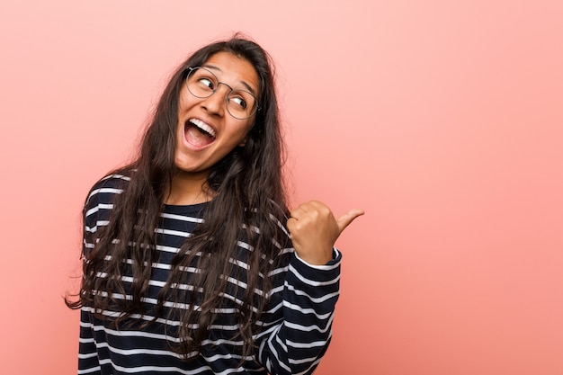 Jonge intellectuele Indiase vrouw wijst met duimvinger weg, lachend en zorgeloos.