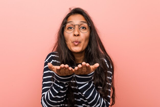 Jonge intellectuele indische vrouw die lippen vouwen en palmen houden om luchtkus te verzenden.