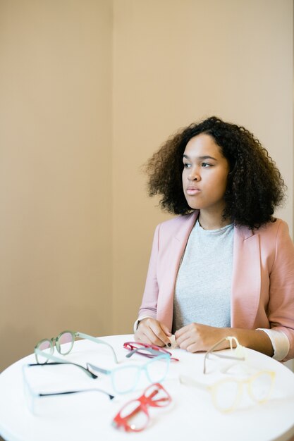 Jonge interculturele vrouw met krullend haar nieuwe bril kiezen in optica winkel of klinieken