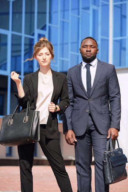 Jonge interculturele zakelijke professionals in formalwear die voor de camera staan tegen het moderne gebouw van de luchthaven tijdens het wachten op de vlucht