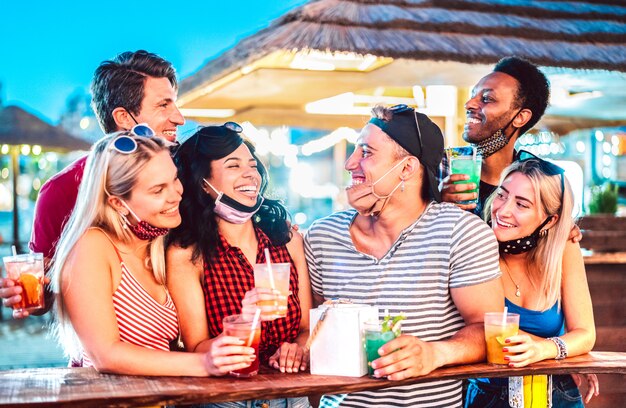Jonge internationale vrienden praten op strand cocktailbar met open gezichtsmasker