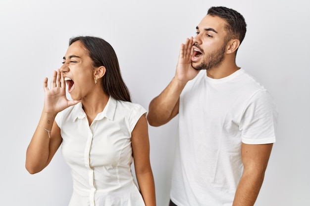 Jonge interraciale paar staande samen verliefd over geïsoleerde achtergrond schreeuwen en schreeuwen luid naar de andere kant met de hand op de mond communicatieconcept