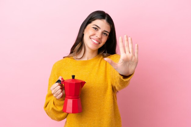 Jonge Italiaanse vrouw met een koffiezetapparaat geïsoleerd op een roze achtergrond die vijf met vingers telt