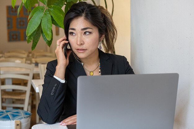 Jonge Japanse vrouwelijke ondernemer zakenvrouw die werkt in een cafetaria met behulp van laptop en smartphone