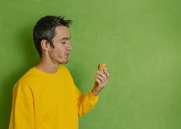 Jonge jongen die een gebeten cupcake bekijkt die hij in zijn hand, groene achtergrond houdt