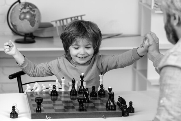 Jonge jongen die schaak speelt met vader en leuke educatieve spelletjes heeft, knappe vader en zoon zijn