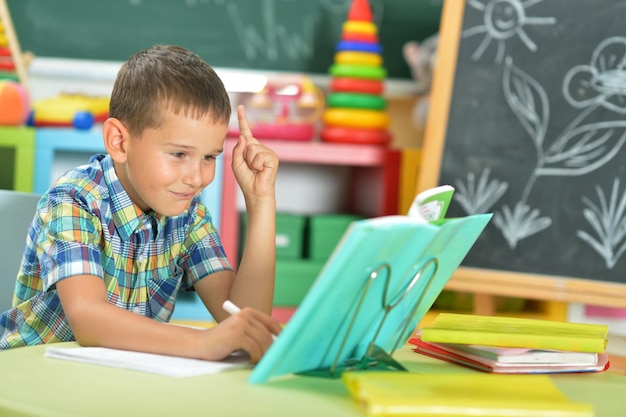 Jonge jongen doet huiswerk en wijst met de vinger omhoog in de klas