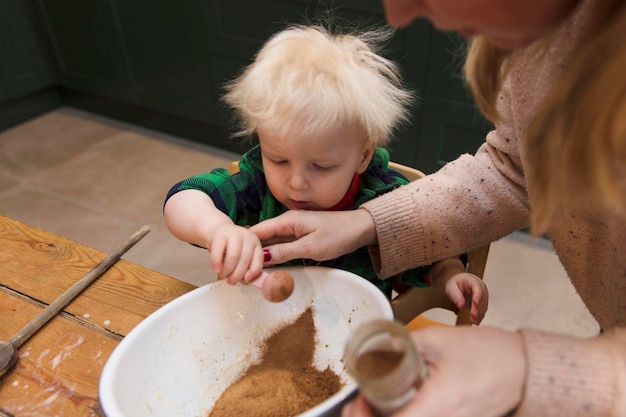 Jonge jongen helpt zijn moeder om ingrediënten toe te voegen aan een mengkom in de keuken