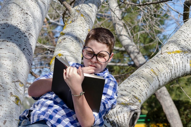 Jonge jongen leest een boek in het bos met ondiepe scherptediepte en kopieerruimte