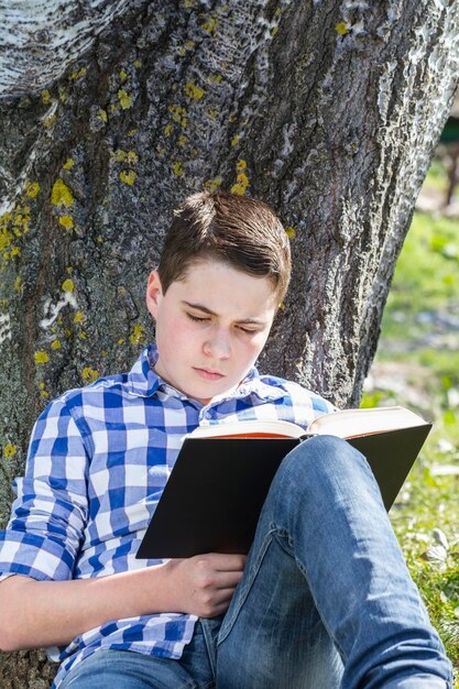 Jonge jongen leest een boek in het bos met ondiepe scherptediepte en kopieerruimte