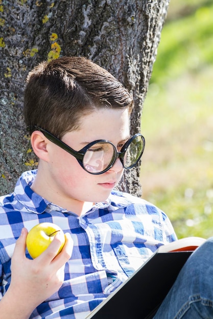 Jonge jongen leest een boek in het bos met ondiepe scherptediepte en kopieerruimte