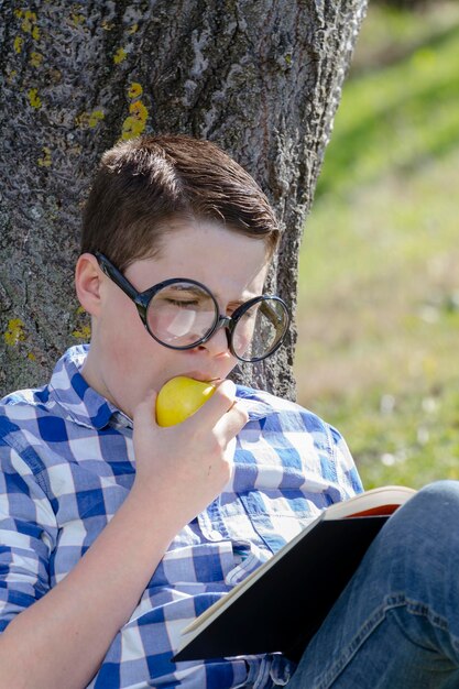 Jonge jongen leest een boek in het bos met ondiepe scherptediepte en kopieerruimte