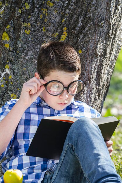 Jonge jongen leest een boek in het bos met ondiepe scherptediepte en kopieerruimte