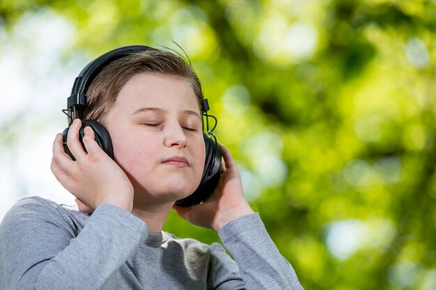 Jonge jongen luistert of geniet van een muziek buiten of park met grote koptelefoon