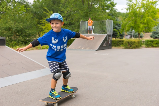 Jonge jongen met beschermende knie- en elleboogbeschermers en een trendy blauwe outfit die op zijn skateboard rijdt in een skatepark en geniet van zijn zomervakantie