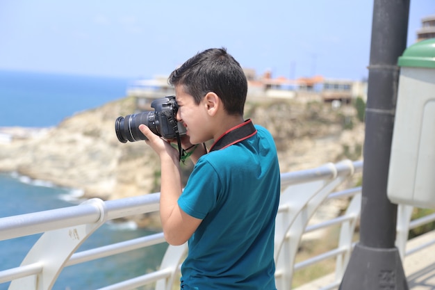 Jonge jongen met camera die een foto maakt op het strand van de zeestad