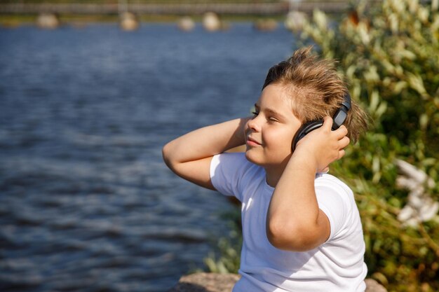 Jonge jongen met koptelefoon luisteren naar muziek aan het meer