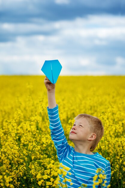 Jonge jongen met papieren vliegtuigje tegen de blauwe hemel