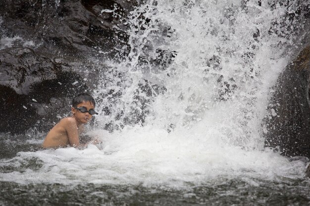 Jonge jongen spelen in natuurlijk water bij waterval