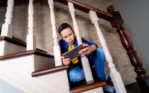 Jonge jongen spelen met smartphone, zittend op de trap. Van onderaf bekijken.