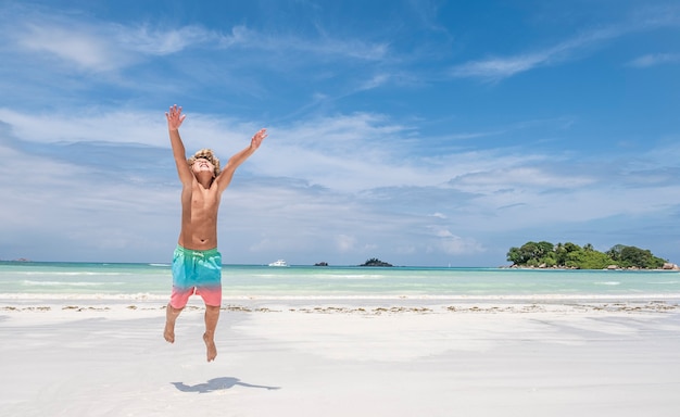 Jonge jongen springen van vreugde op tropisch strand, concept van de zomervakantie