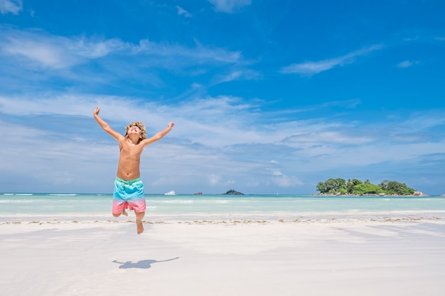 Jonge jongen springen van vreugde op tropisch strand en eiland achtergrond, concept van de zomervakantie