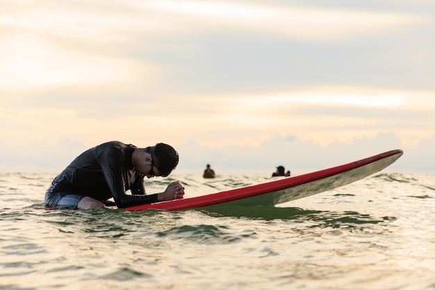 Foto jonge jongen tiener surfboarder buigt zijn hoofd in uitputting moe en teleurgesteld tijdens het leren en oefenen van surfen