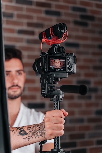 Jonge jongen van in de twintig die het camerastatief in zijn studio aanpast