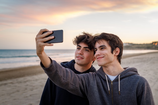 jonge jongens die op het strand zitten en foto's maken met hun mobiele telefoons