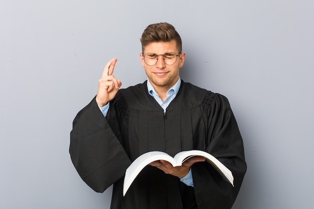 Jonge jurist die een boek houdt dat vingers kruist voor het hebben van geluk