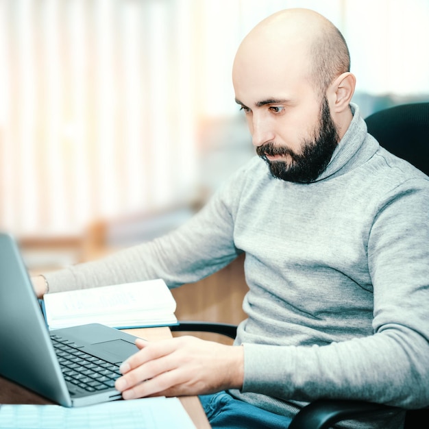 Jonge kale en bebaarde man van 2535 jaar oud werkt op kantoor voor laptop Man in vrijetijdskleding kijkt naar laptopmonitor