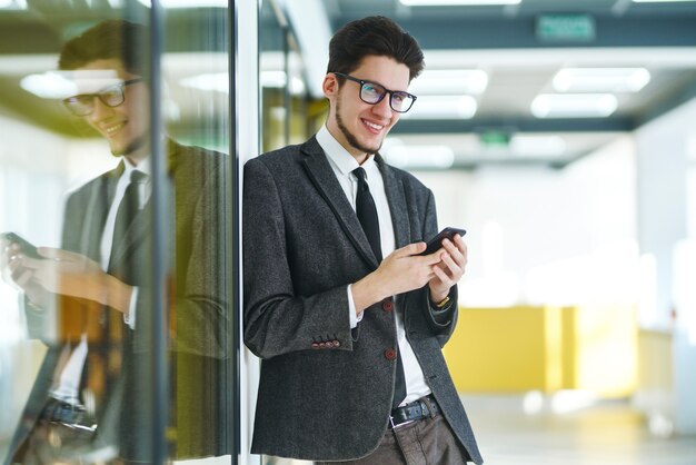 Jonge kantoormedewerker in glazen met behulp van mobiele slimme telefoon. Zakenman houdt telefoon in de hand.