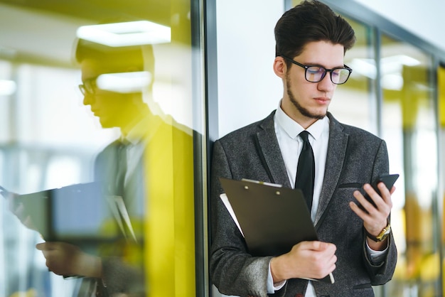 Jonge kantoormedewerker in glazen met behulp van mobiele slimme telefoon Zakenman houdt telefoon in de hand