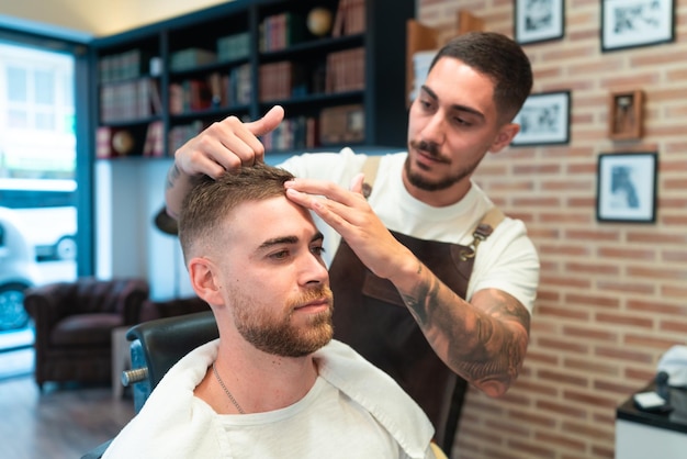 Jonge kapper met tatoeages die het haar van de mannelijke klant in een kapsalon stylen