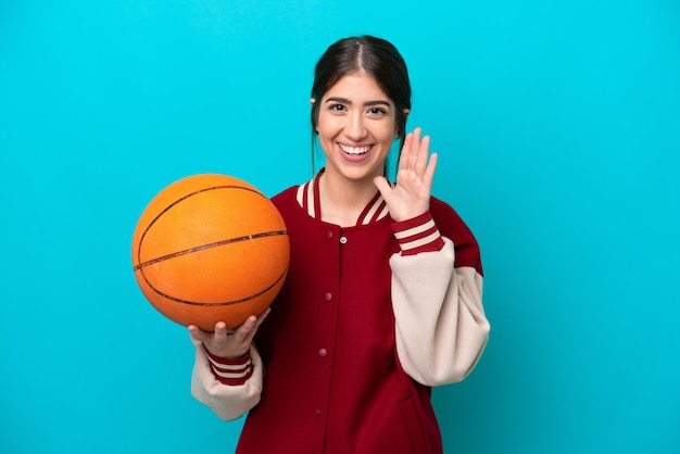 Jonge kaukasische basketbalspelervrouw die op blauwe achtergrond wordt geïsoleerd die met wijd open mond schreeuwt