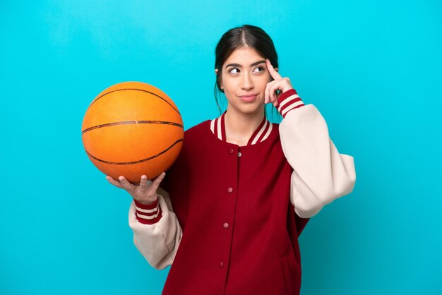 Jonge kaukasische basketbalspelervrouw die op blauwe achtergrond wordt geïsoleerd die twijfels heeft en denkt