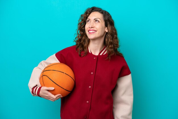 Jonge kaukasische basketbalspelervrouw die op blauwe achtergrond wordt geïsoleerd en een idee denkt terwijl ze omhoog kijkt